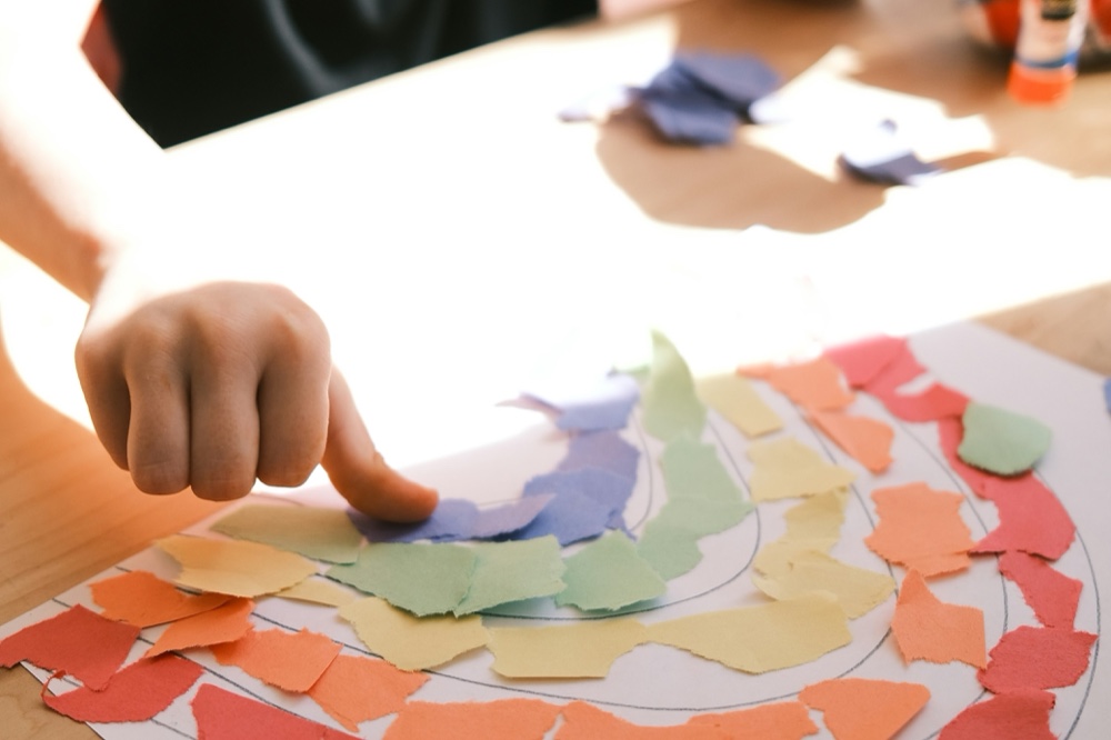 A child arranging torn paper into a rainbow