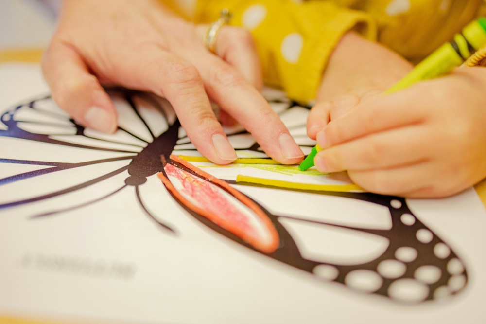 An adult's hands guiding a child's hands over a colouring page